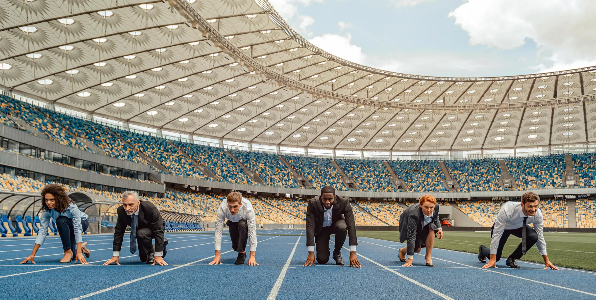 Kolleginnen und Kollegen in Business-Kleidung an der Startlinie in einem Stadion
